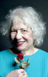 Aviva Cantor wearing a blue shirt holding a rose and smiling to the camera