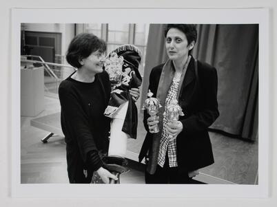 Miriam Rosengarten holding a Torah, partially removing its cover, and Rina Otterbach holding two Torah crowns
