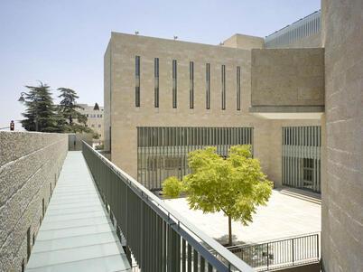 A minimalist building of tan stone, with a small courtyard and a tree