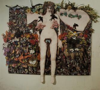 art work with a pale female figure surrounded by plastic and fabric flowers and colorful ornaments