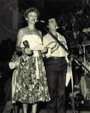 Rosete Rubin and Herri Rosemberg standing on stage at two microphones, surrounded by a crowd of people