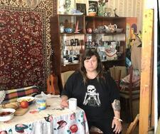 Zoya Cherkassky sitting at a table in a room with china shelves and a Persian rug wall hanging