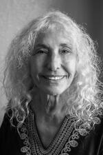 black and white photograph of a woman with long curly white hair smiling at the camera