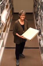 Woman standing holding large box, library shelves in background