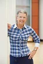 Deborah Dash Moore leaning against wall, blue plaid shirt, short gray hair, glasses