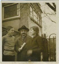 Black and white photograph of a man with a mustache and a hat looking at the camera, with a girl on one side and a boy on the other looking at him