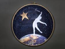 Embroidery hoop depicting a woman's silhouette on a navy background on the arc of planet Earth reaching toward toward a star