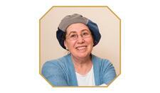 photograph of a woman with glasses with a loose hat as a head covering, smiling at the camera
