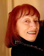 photgraph of a woman with red hair looking over her shoulder at the camera with a smile on her face