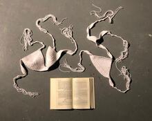 Installation of crocheted white bra and underwear with a prayer book, on a dark background