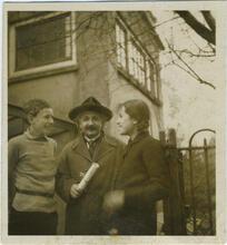 Black and white photograph of a man with a mustache and a hat looking at the camera, with a girl on one side and a boy on the other looking at him