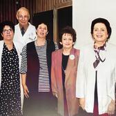 Six women and one man standing together, four wearing white doctor's coats