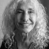 black and white photograph of a woman with long curly white hair smiling at the camera