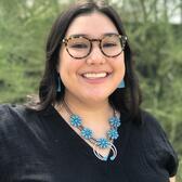 photograph of a woman with glasses and long dark hair wearing turquoise necklace