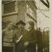 Black and white photograph of a man with a mustache and a hat looking at the camera, with a girl on one side and a boy on the other looking at him
