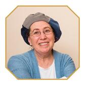 photograph of a woman with glasses with a loose hat as a head covering, smiling at the camera