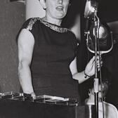 black and white photograph of a woman in a dark dress at a microphone