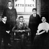 Sonja Schlesin with Gandhi and three others in front of a window reading M.K. Gandhi Attorney