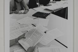 A group of women sitting at some tables pushed together, reading packets of paper