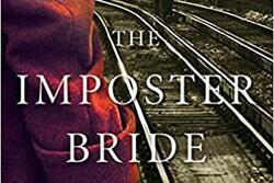 Close photograph of a woman’s arm, in a red wool coat, holding a suitcase beside train tracks