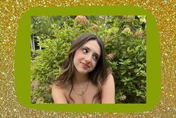 Image of Eva smiling and wearing gold necklaces with flowers in background