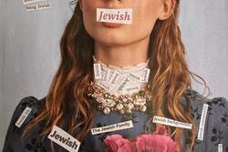 A woman with a calm expression wears labels reading "Jewish" on her face and blue dress. The dress features a large pink flower, intricate detailing, and conveys themes of identity.