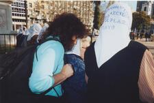 photograph of a woman with dark curly hair and a back pack seen from the side, with other women with white kerchiefs marching