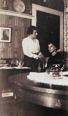 black and white photograph of one woman standing and another sitting at a table