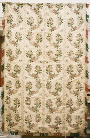 An off-white curtain embroidered with pink flowers, with fringe along the edges
