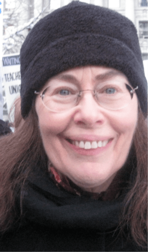 photograph of a woman looking at the camera and smiling wearing a dark hat