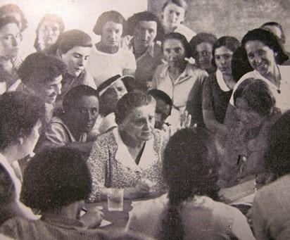 A large group of women crowded around a table, with Puah Rakovsky in the center