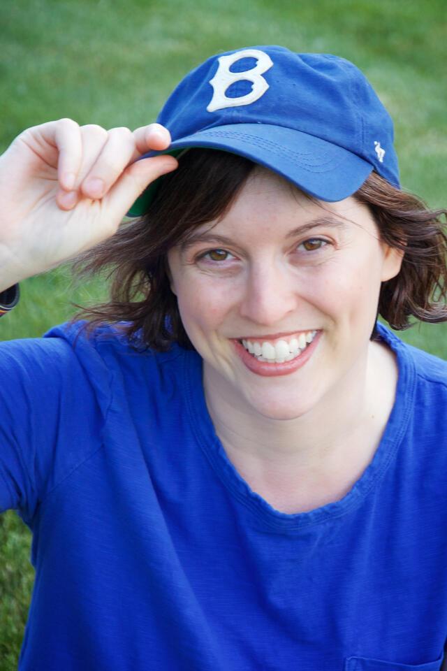 Jessie Atkin wearing blue t-shirt and blue baseball cap posing in front of grass