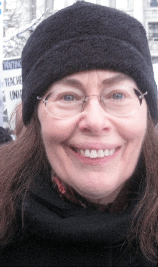 photograph of a woman looking at the camera and smiling wearing a dark hat