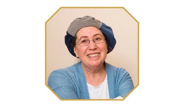 photograph of a woman with glasses with a loose hat as a head covering, smiling at the camera