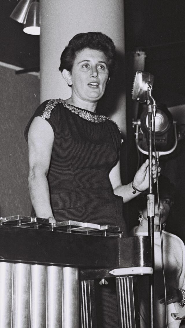 black and white photograph of a woman in a dark dress at a microphone