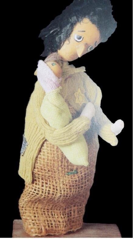 photograph of a doll with black hair, wearing a burlap dress with a yellow star and holding a baby doll
